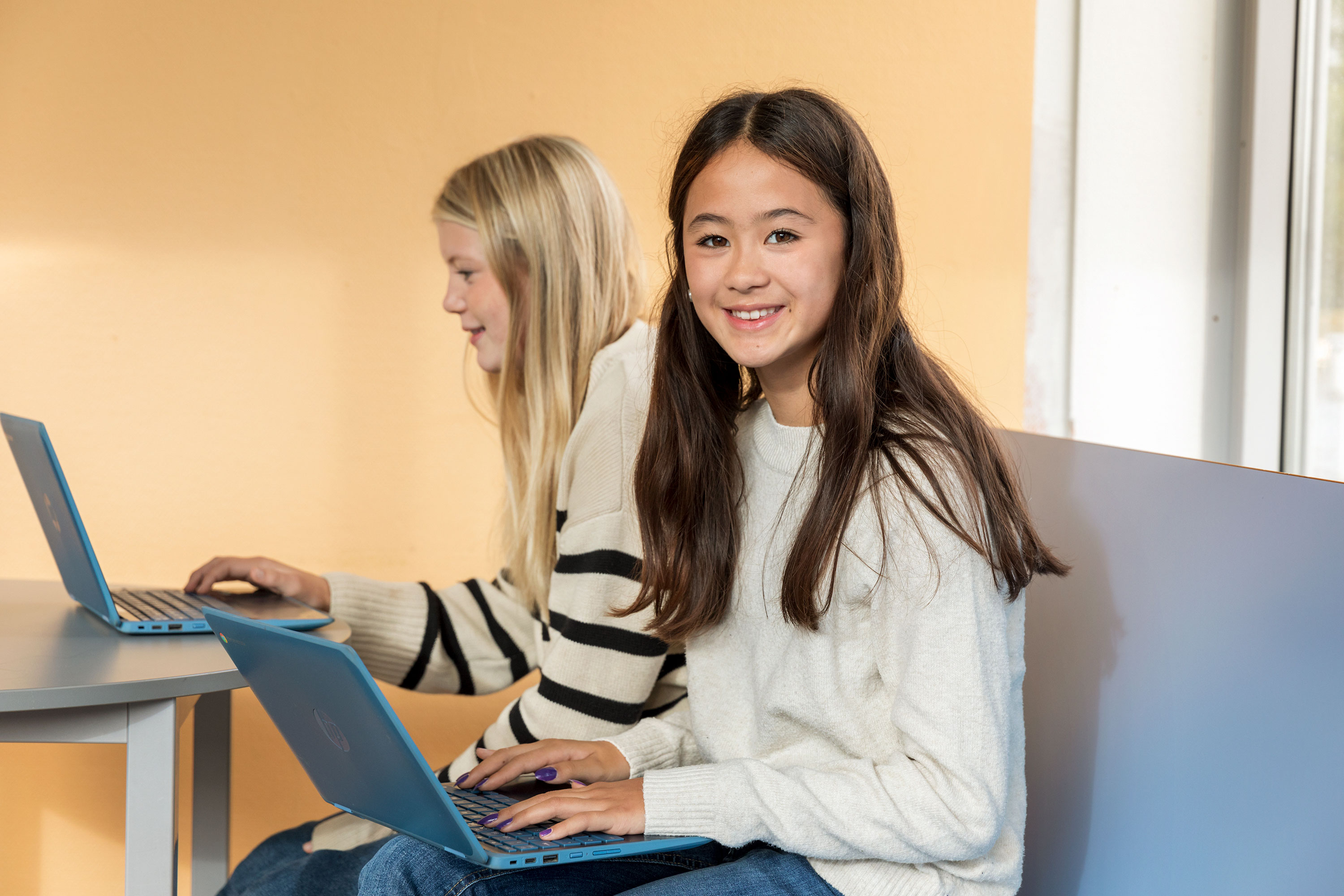 Två elever sitter i ett klassrum med en varsin dator.